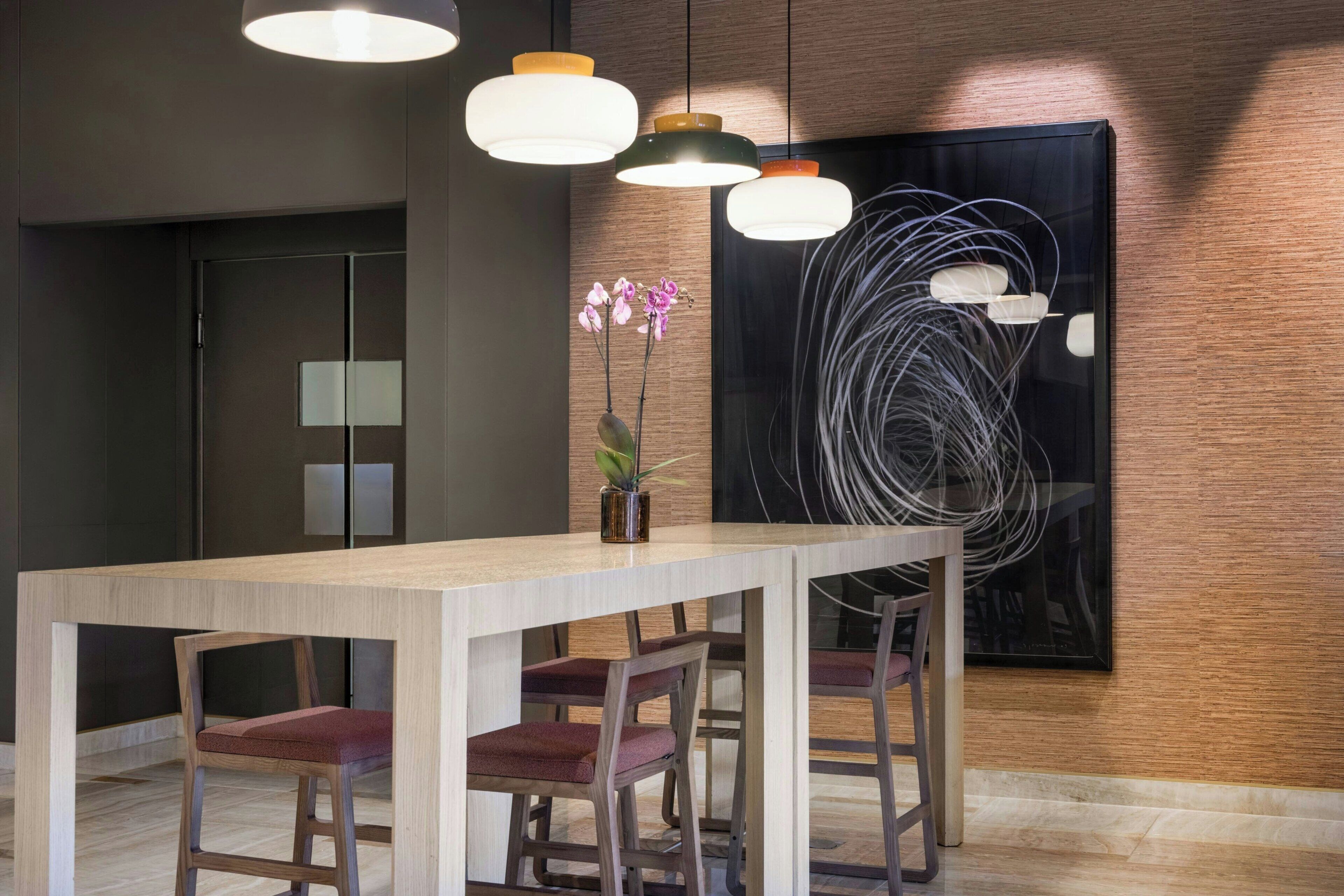 Un comedor moderno con mesa y sillas de madera, iluminación colgante y un cuadro abstracto grande en la pared.