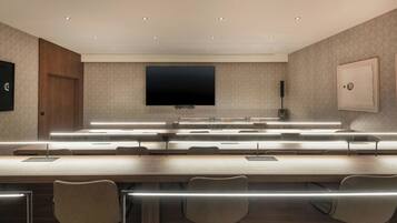 Une salle de conférence équipée d’un grand téléviseur à écran plat, de plusieurs tables avec des chaises et d’un éclairage encastré au plafond.