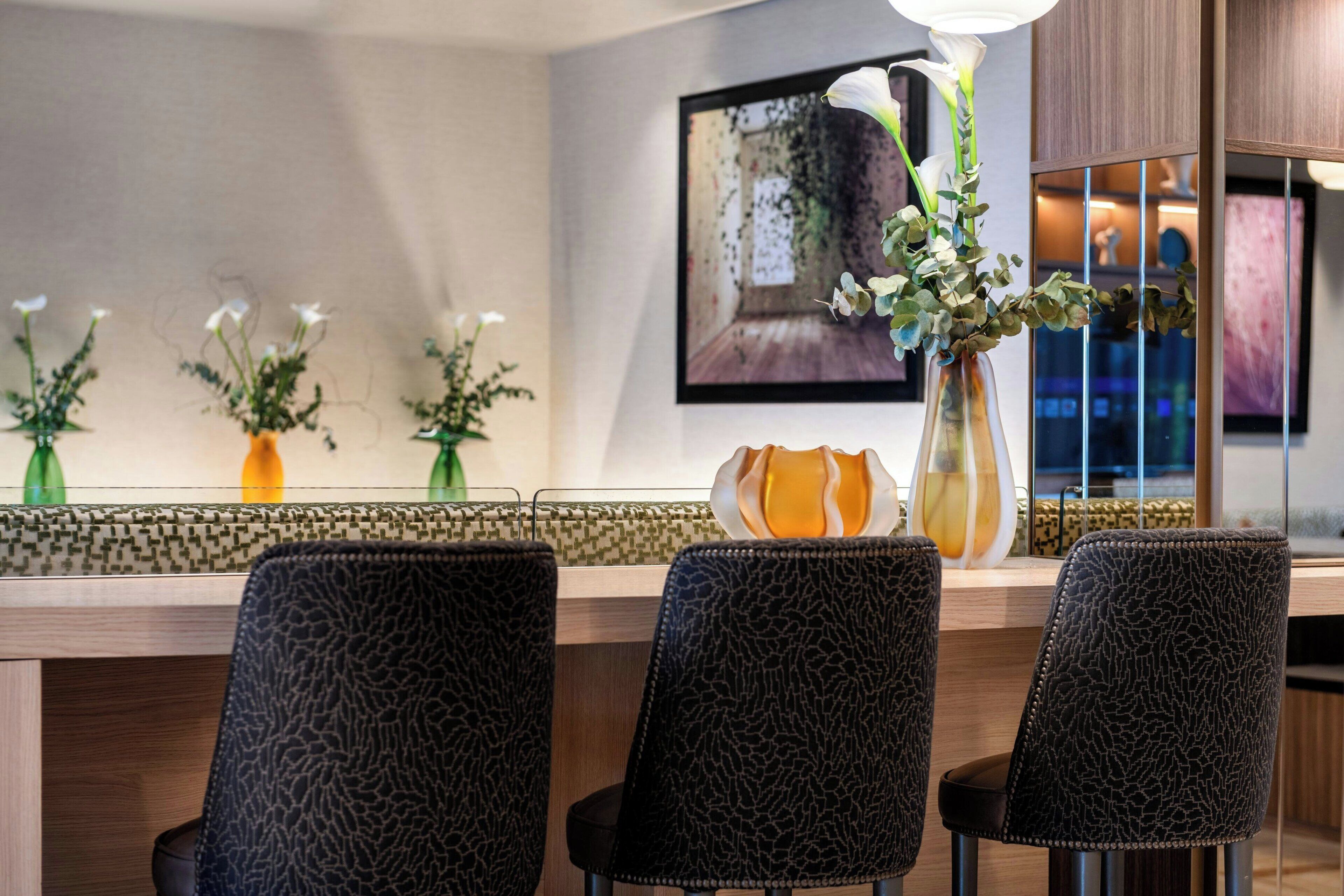 A modern bar area with three chairs, a vase with flowers, and a framed picture on the wall.