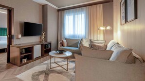 A hotel room with a flat-screen TV, a sofa, a coffee table, a desk with a lamp, and a bed. - AC Hotel Bologna by Marriott (Bologna)