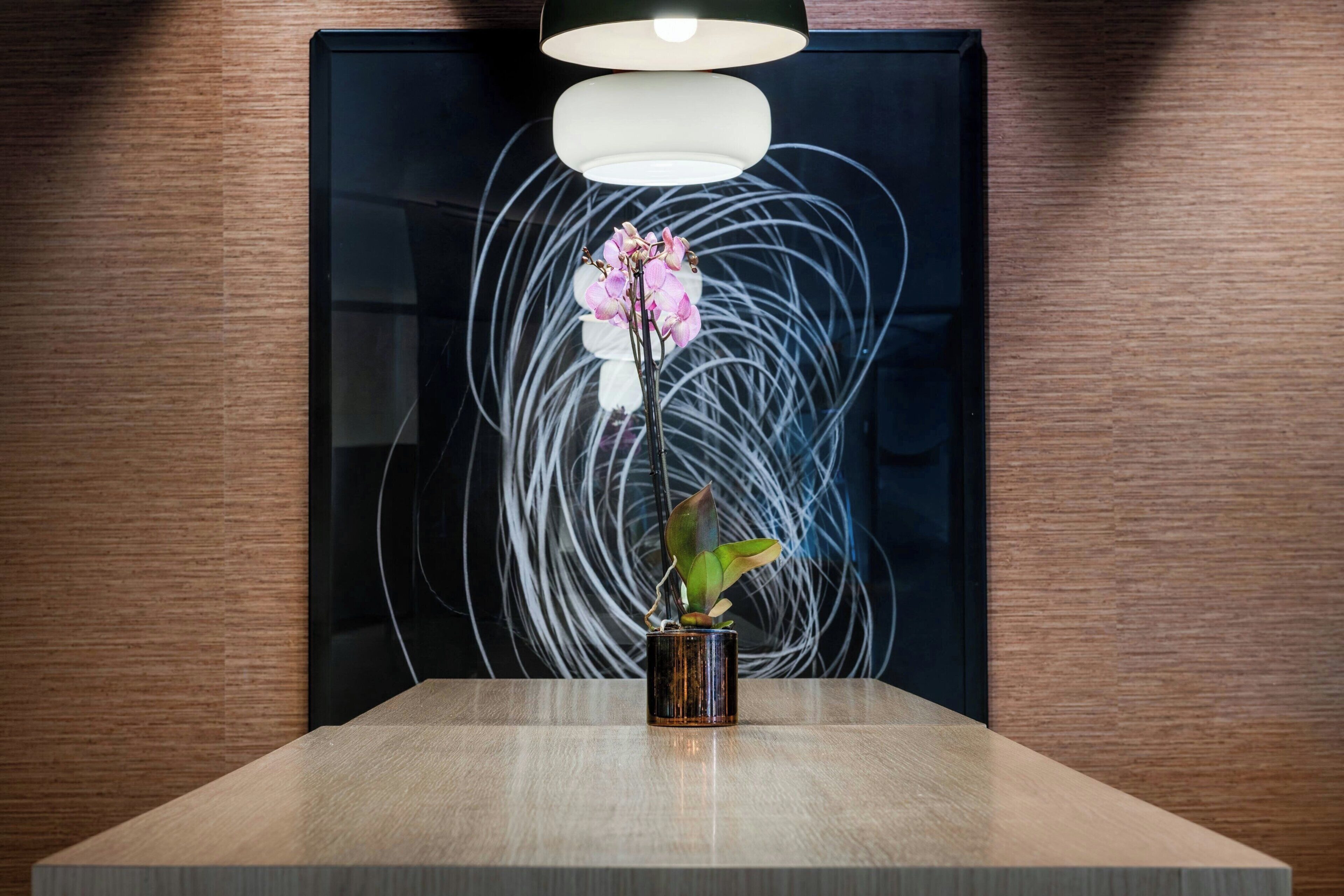 Una mesa moderna con un jarrón de orquídeas rosadas y una planta en maceta.