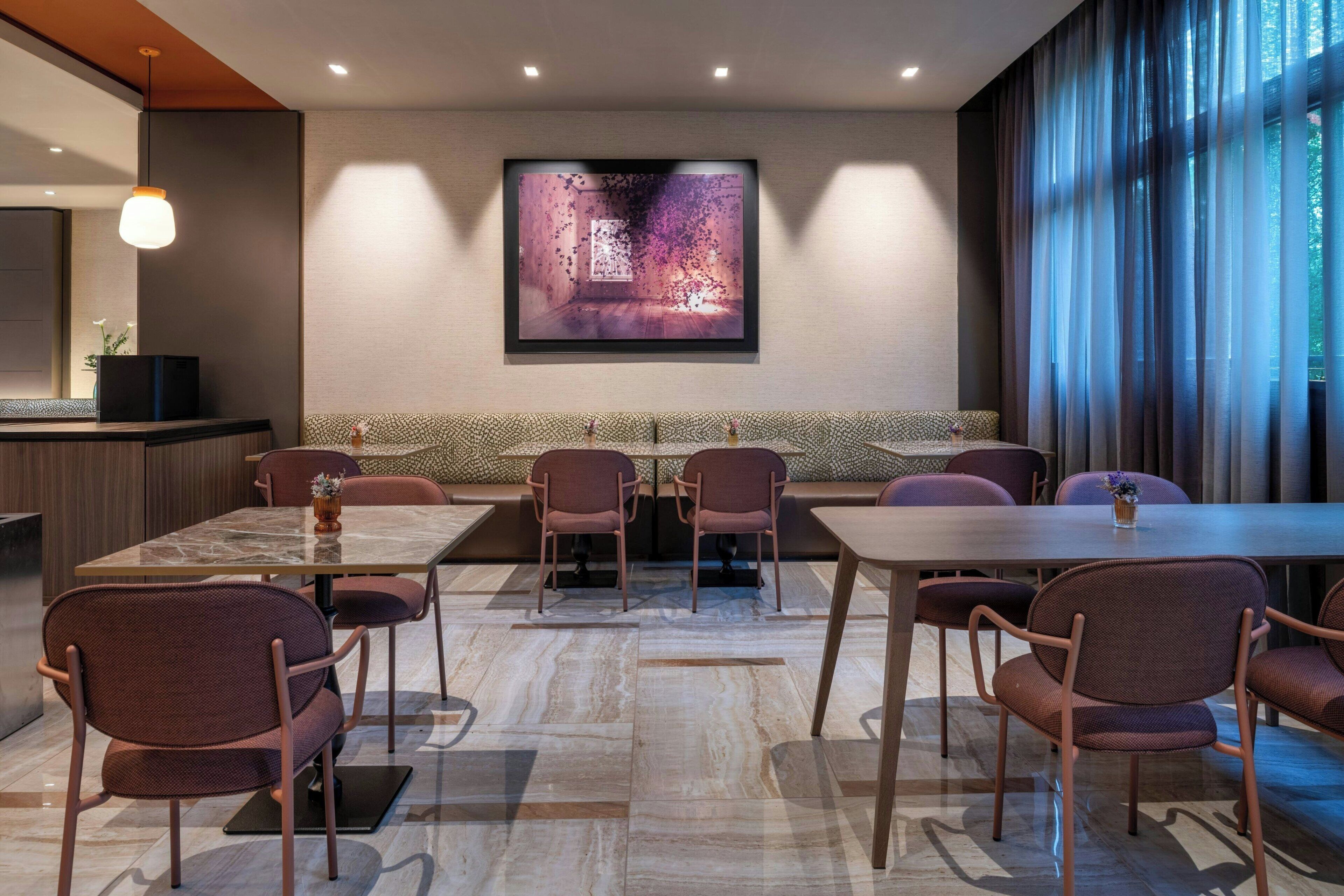 A modern dining area with a marble floor, cushioned seating, and a large framed artwork on the wall.