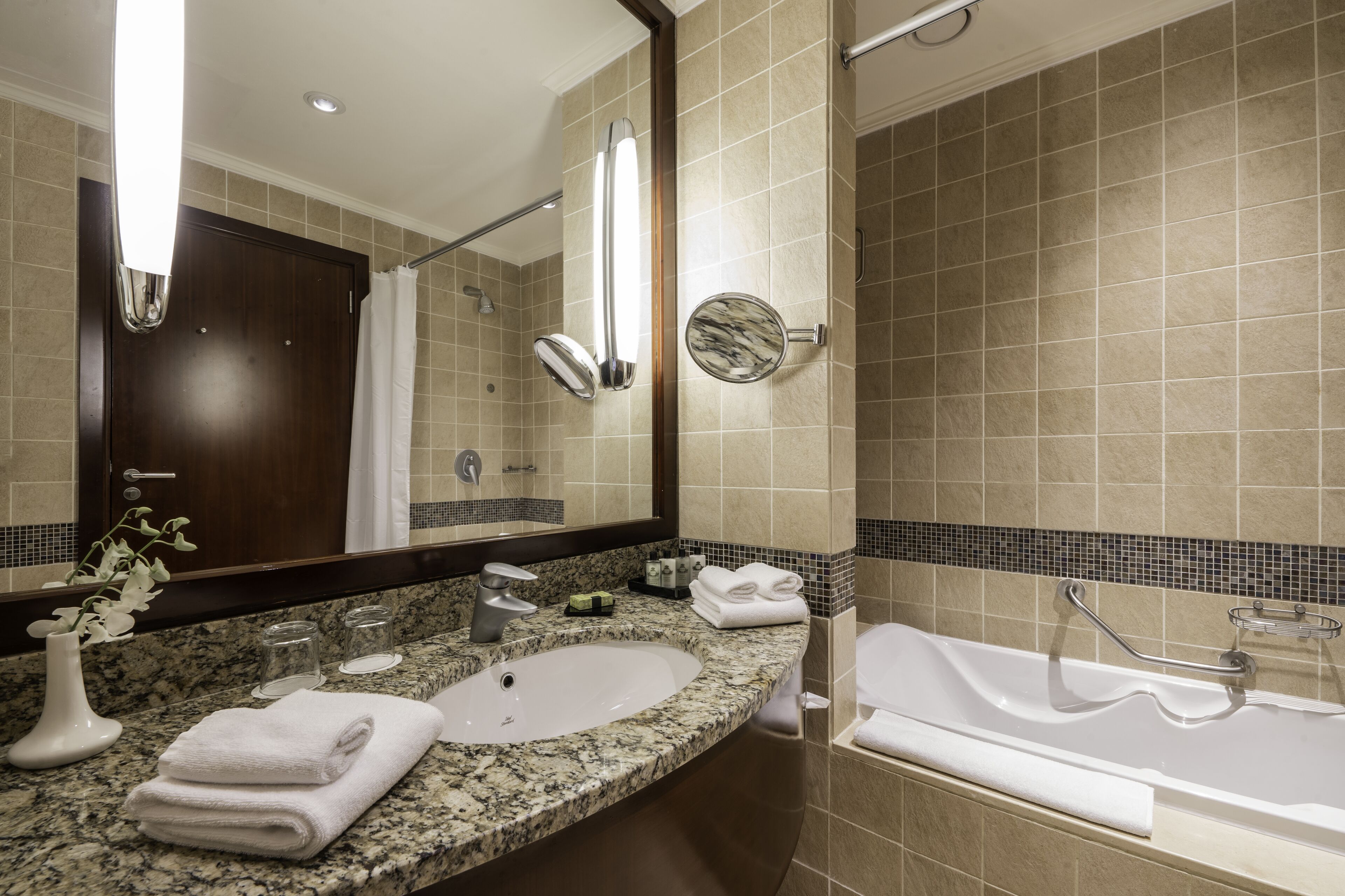 Un baño moderno con encimera de granito, dos lavamanos, un espejo grande y una bañera.