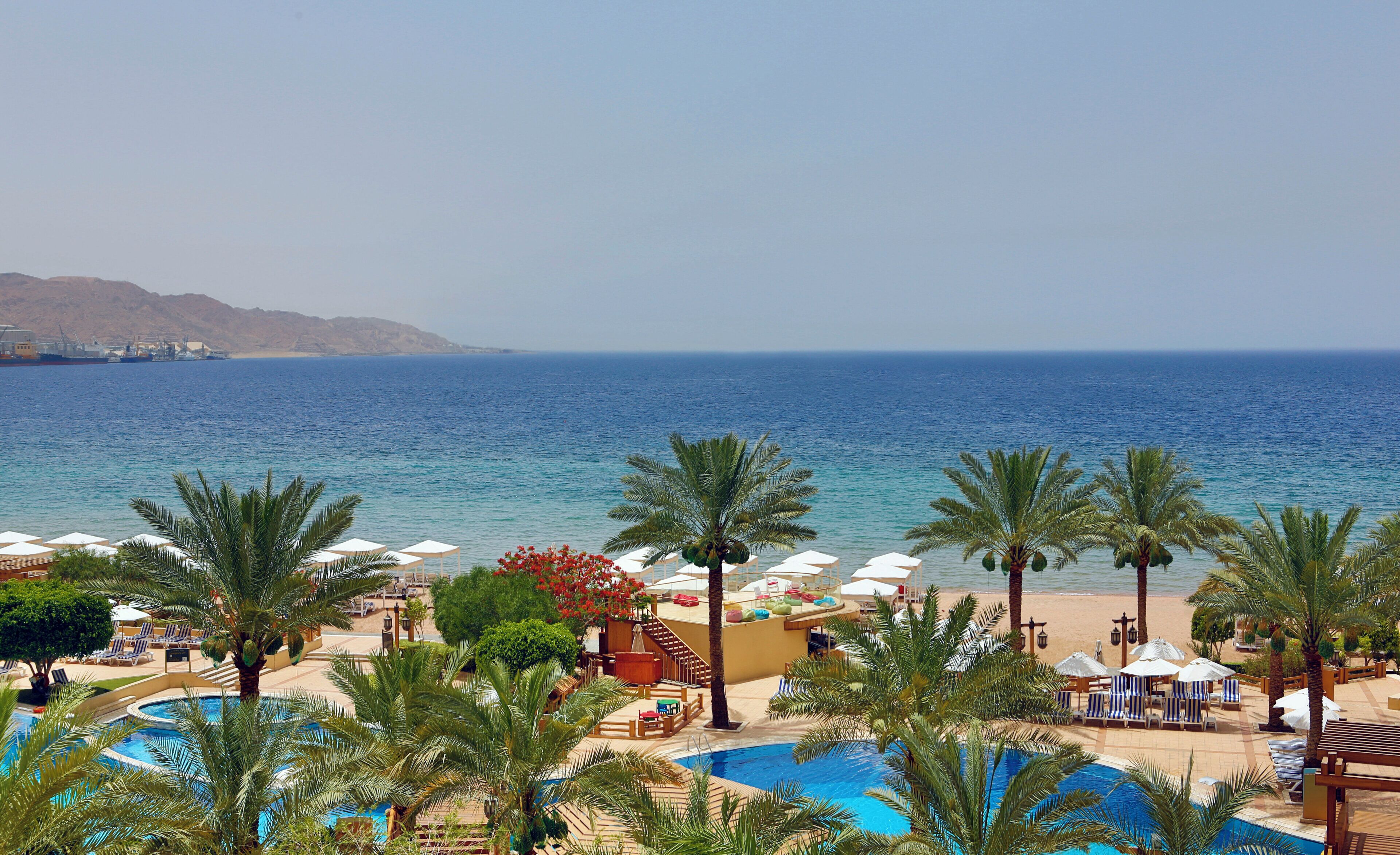 Un complexe hôtelier doté d’une piscine, de chaises de plage, de parasols et offrant une vue sur la mer.