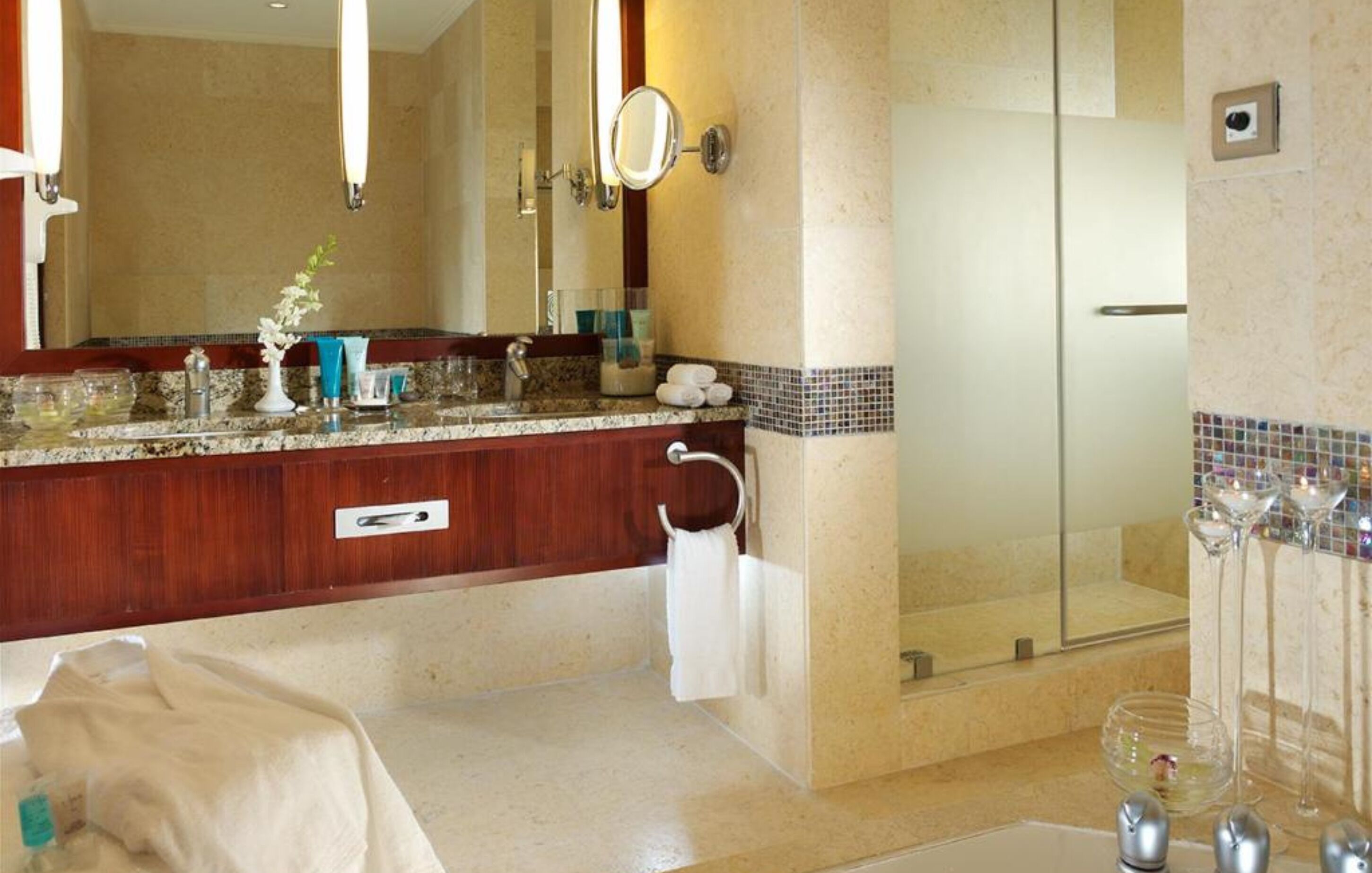 A modern bathroom with a marble vanity, a large mirror, a glass shower enclosure, and a glass-topped vanity.
