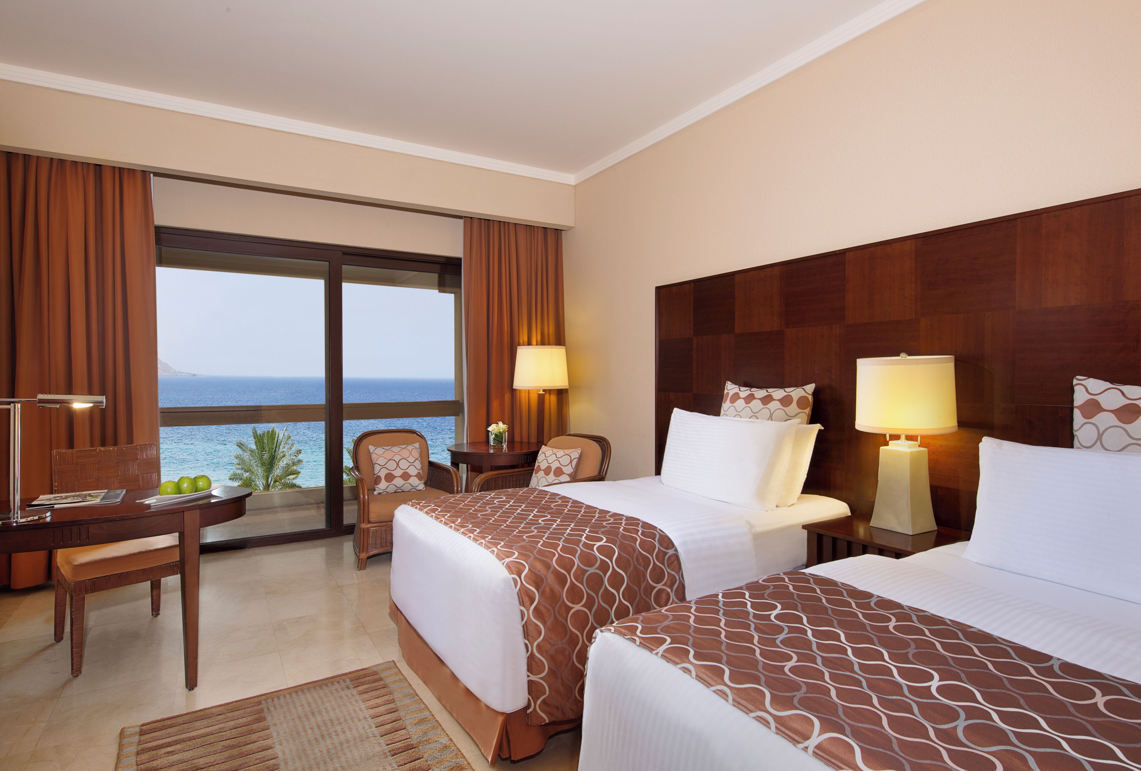 A hotel room with a bed, a desk, a chair, and a view of the sea.