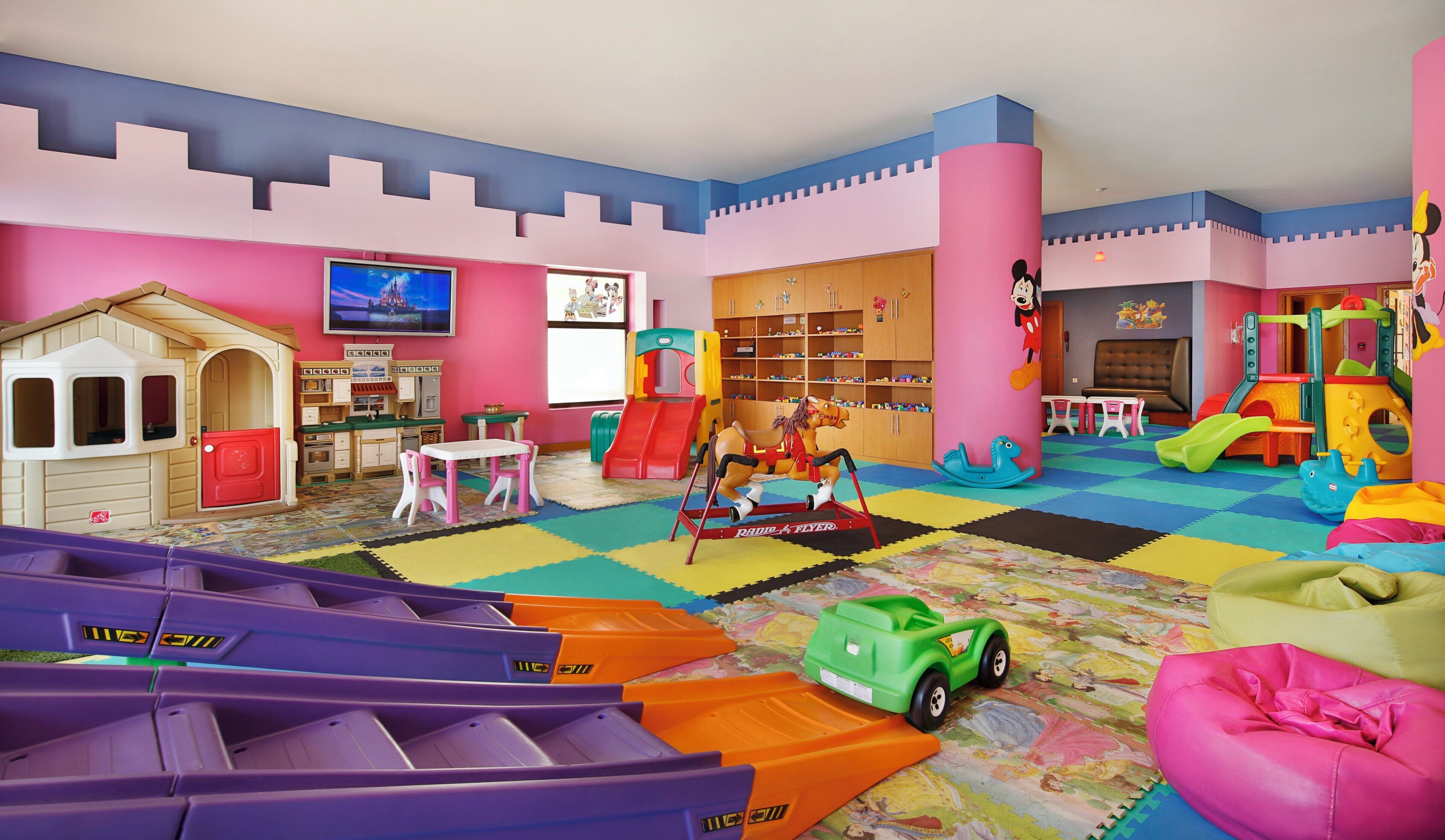 A children's playroom with a playhouse, a slide, a play kitchen, and various toys.