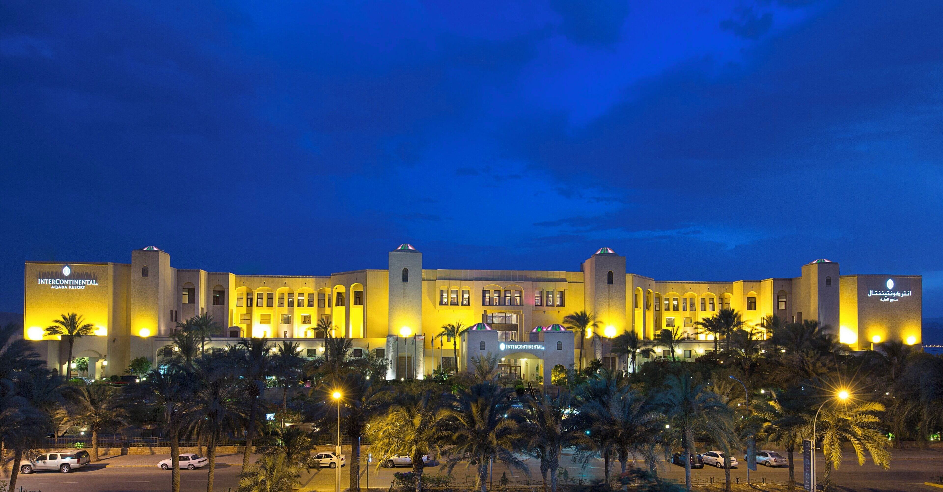 A large hotel with multiple wings, palm trees in the foreground, and a clear sky.