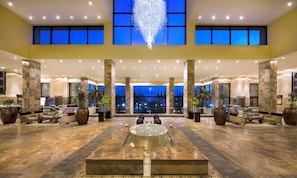 A spacious lobby with a central water feature, seating areas, and large windows offering views of the night sky.