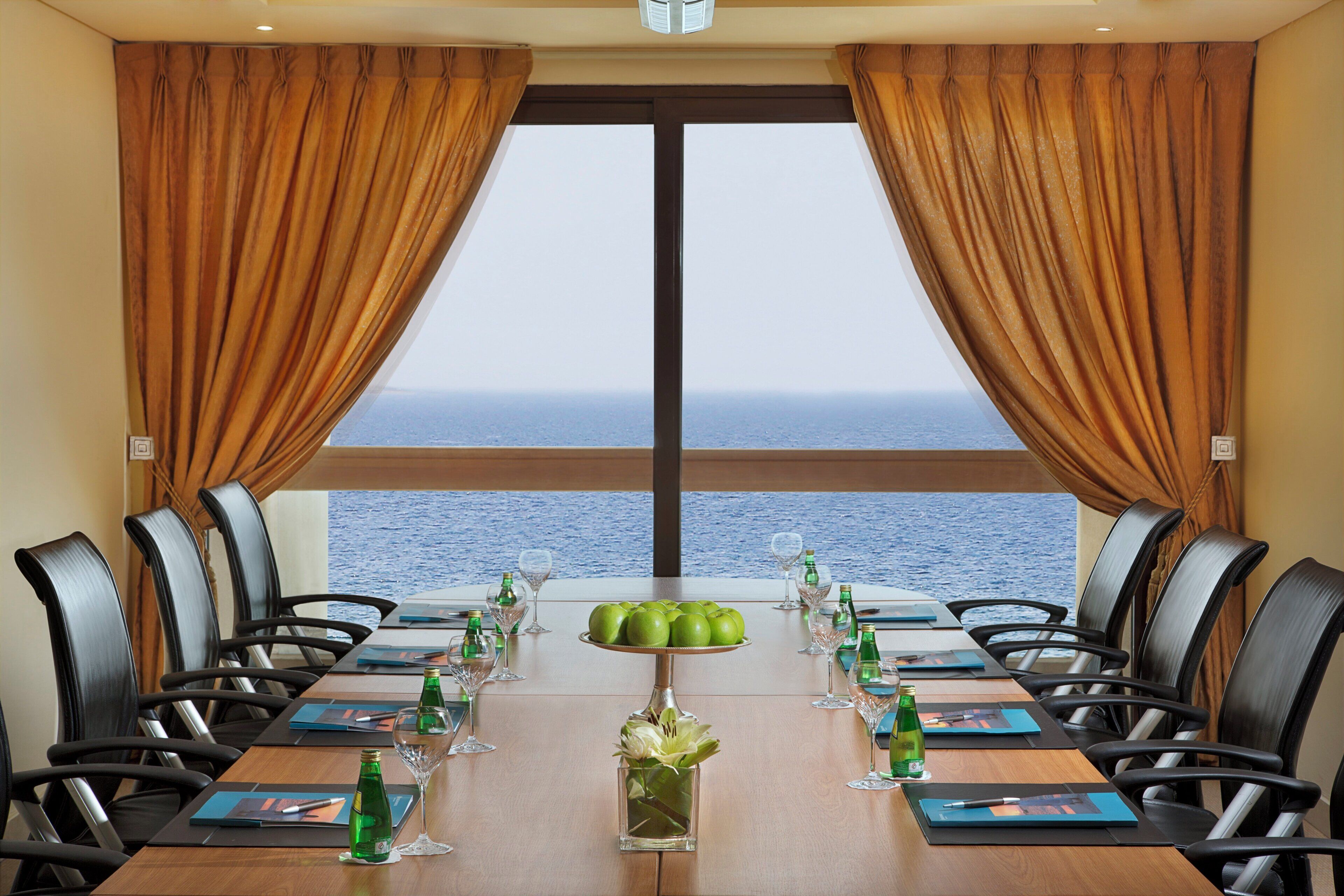 A conference room with a view of the sea, equipped with tables, chairs, and meeting materials.