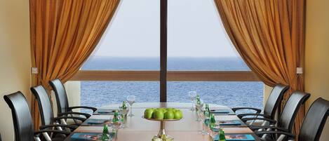 A conference room with a view of the sea, equipped with tables, chairs, and meeting materials.