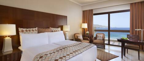 Habitación de hotel con una cama grande, dos sillas, un escritorio y vista al mar.