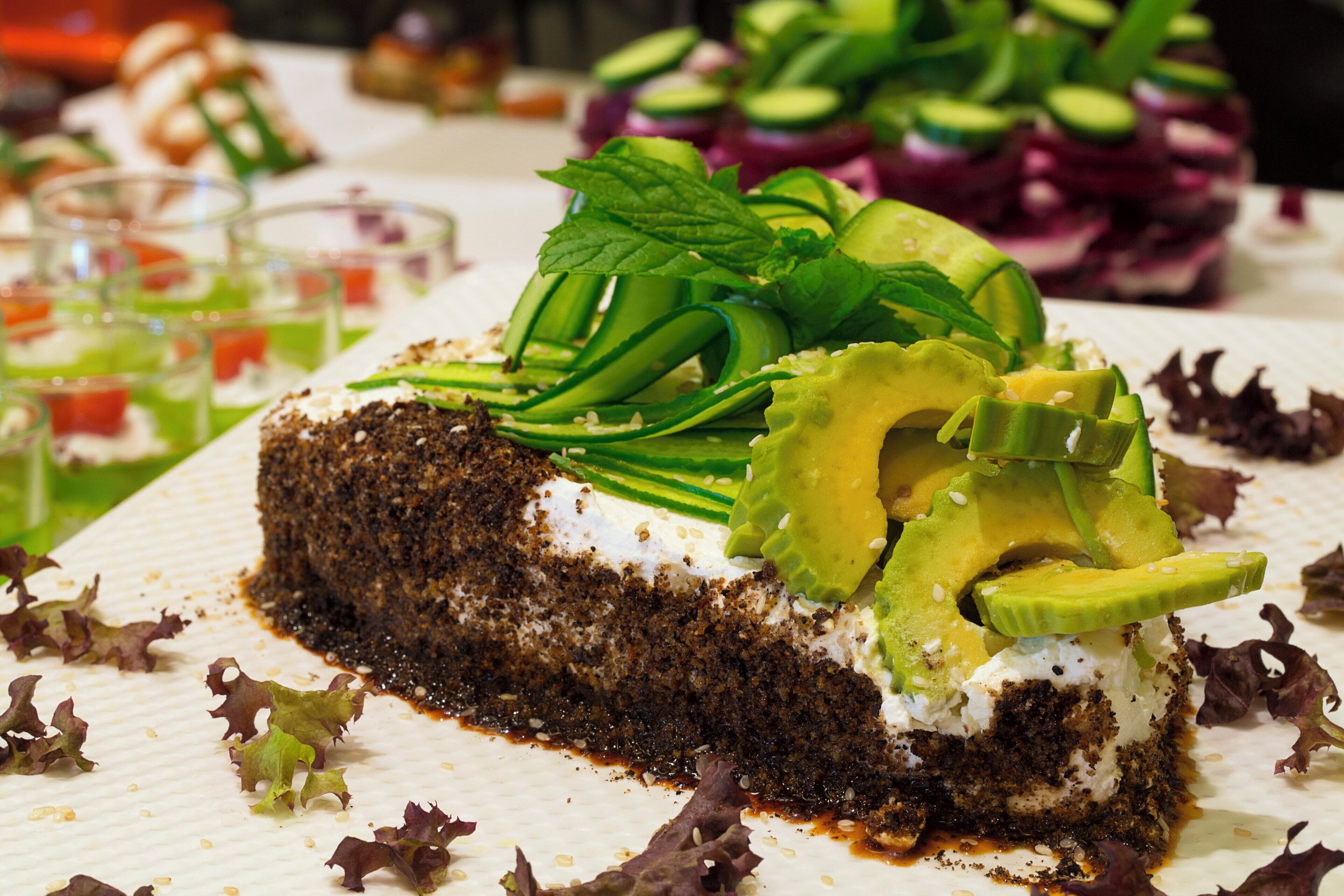 A slice of cake with avocado and greens on a white plate.