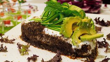A slice of cake with avocado and greens on a white plate.