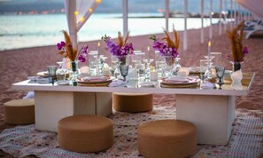 Une table dressée pour deux, installée sur la plage, avec de la vaisselle, des assiettes et des bougies, créant une ambiance propice à un dîner romantique.