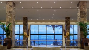 A spacious lobby with large windows offering a view of the sea, stone pillars, and a central water feature.