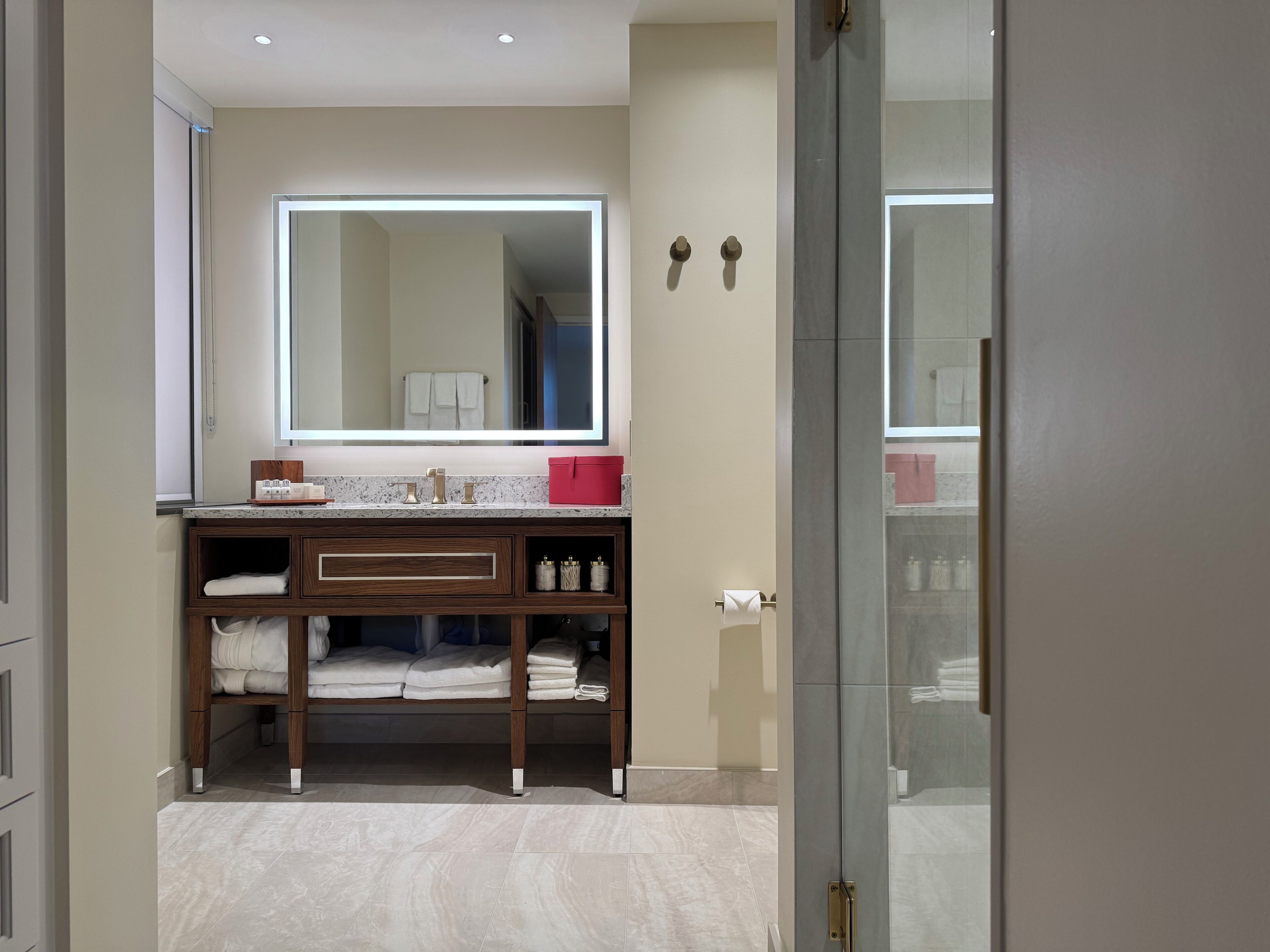 A modern bathroom with a large mirror, wooden vanity, and neatly arranged towels.