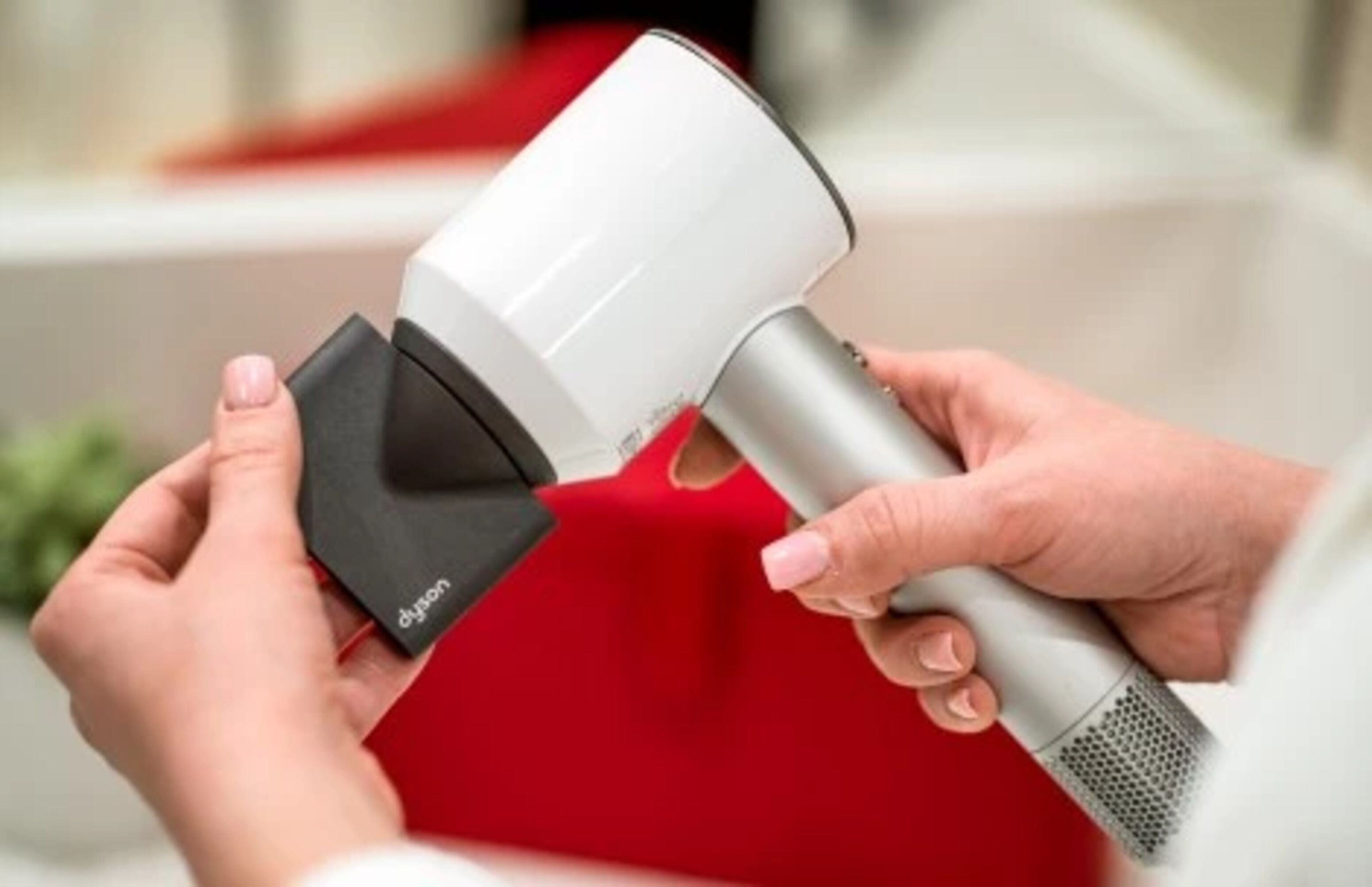 A person holding a Dyson hair dryer with a red cushion in the background.