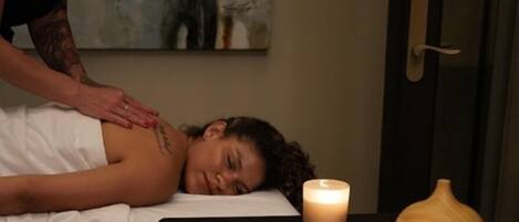 A massage therapy session in a room with a massage table, two lit candles, and a decorative vase.