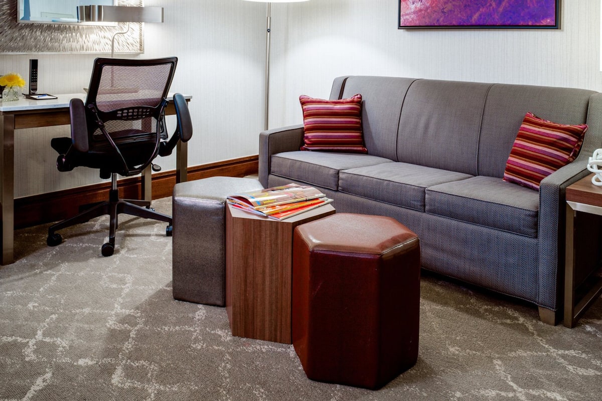 A modern living room with a grey sofa, two striped pillows, a wooden coffee table, a black office chair, and a small side table with a plant.