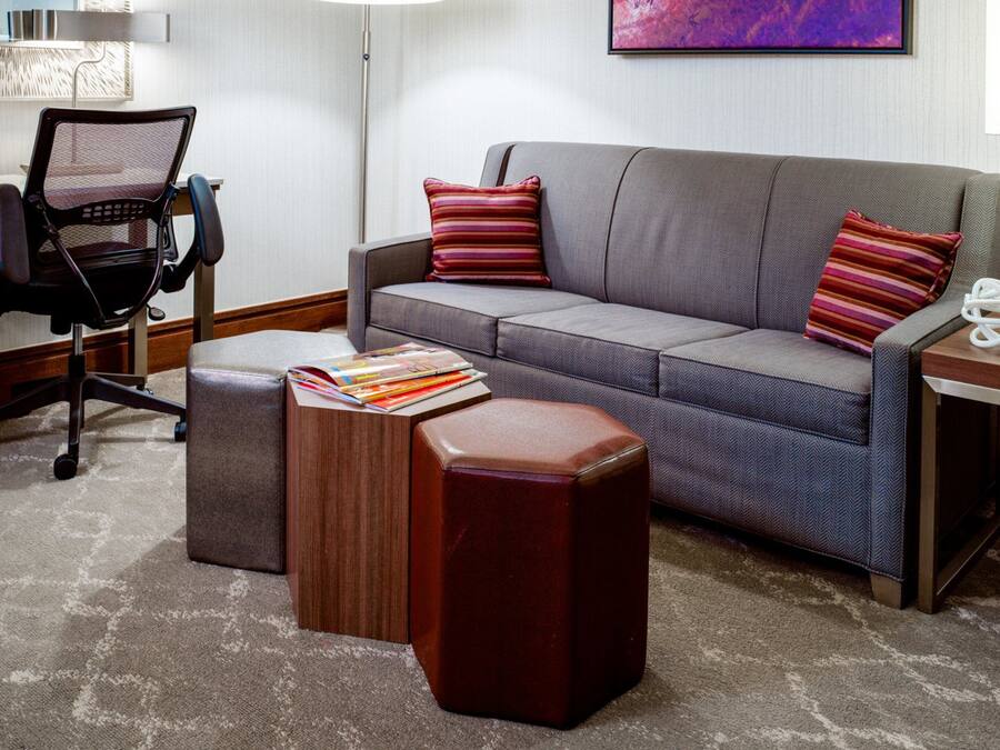 Una sala moderna con un sofá gris, dos almohadas a rayas, una mesa de centro de madera, una silla de oficina negra y una mesita auxiliar con una planta.