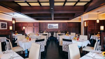 A restaurant with multiple tables, each set with white tablecloths, chairs, and candles.
