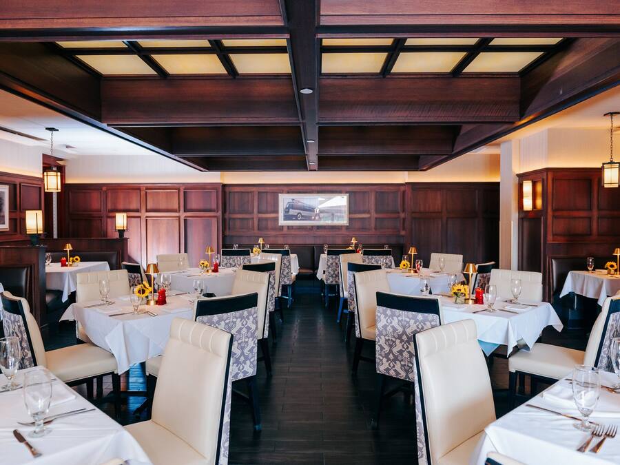 Ein Restaurant mit mehreren Tischen, jeweils gedeckt mit weißen Tischdecken, Stühlen und Kerzen.