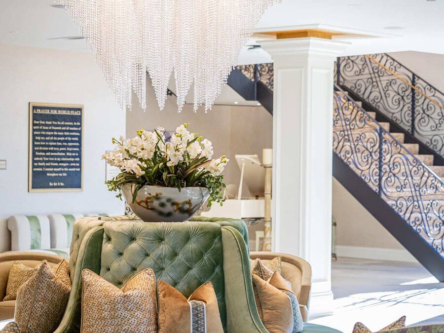 Un salon luxueux avec un grand canapé vert, des fauteuils à motifs, une petite table ronde et un lustre.