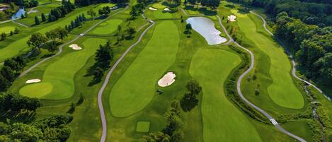 An aerial view of a golf course with multiple holes, sand bunkers, and a pond.