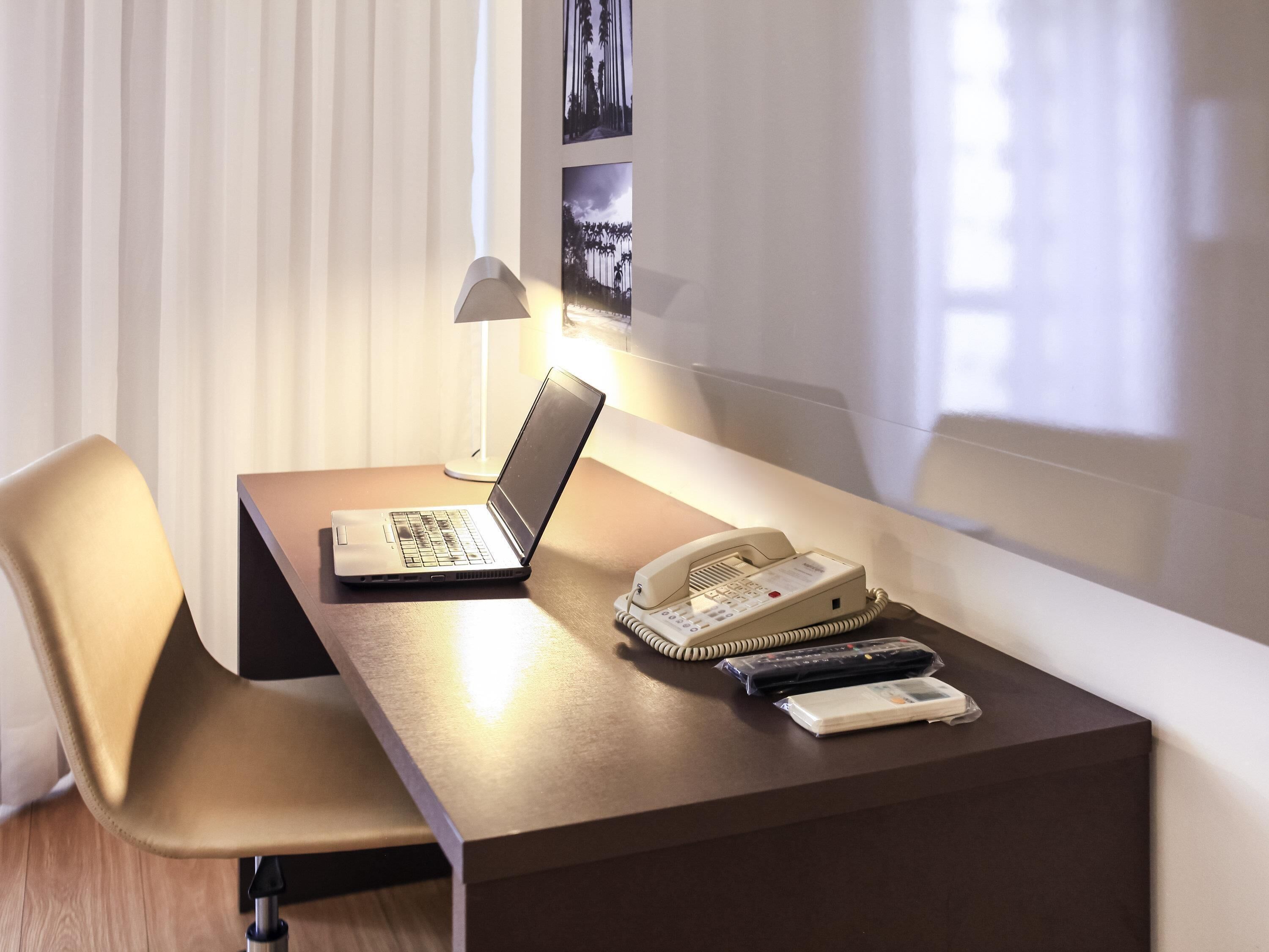 Une chambre d’hôtel équipée d’un bureau, d’un ordinateur portable, d’un téléphone et d’une télécommande.