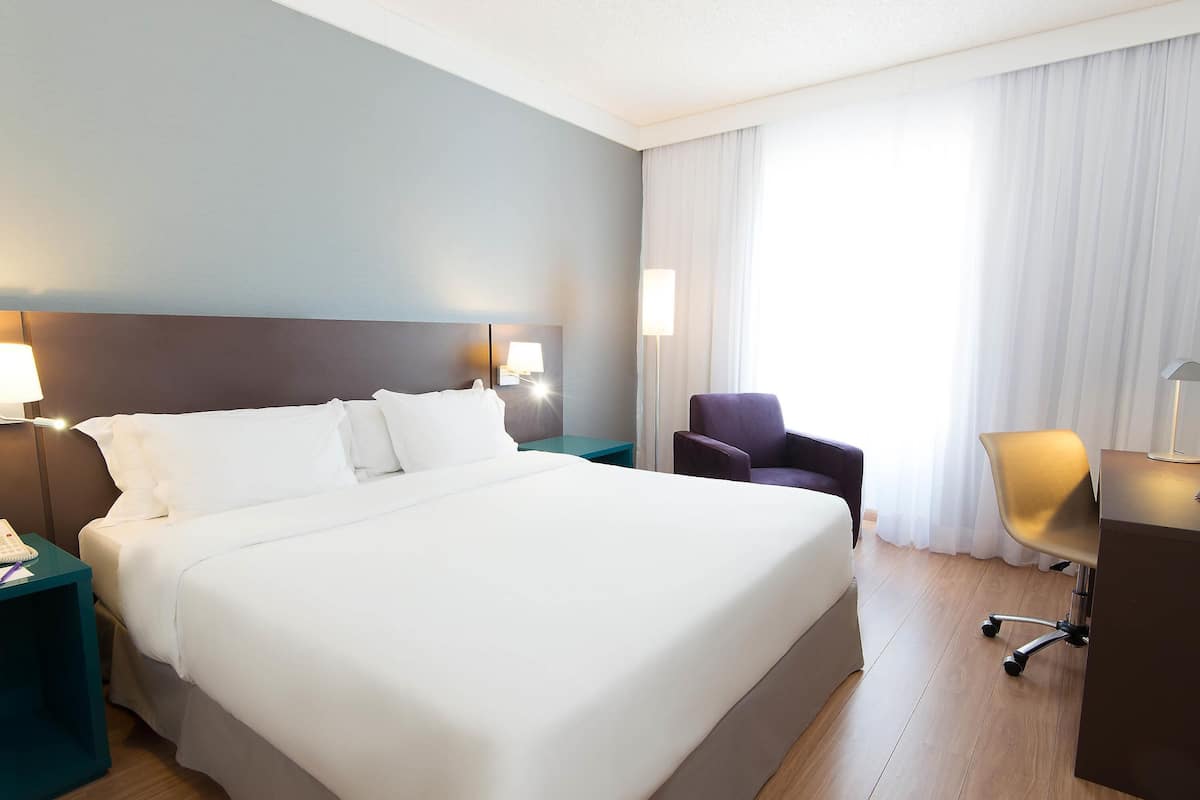 A hotel room with a large bed, a desk, a chair, and two bedside lamps.