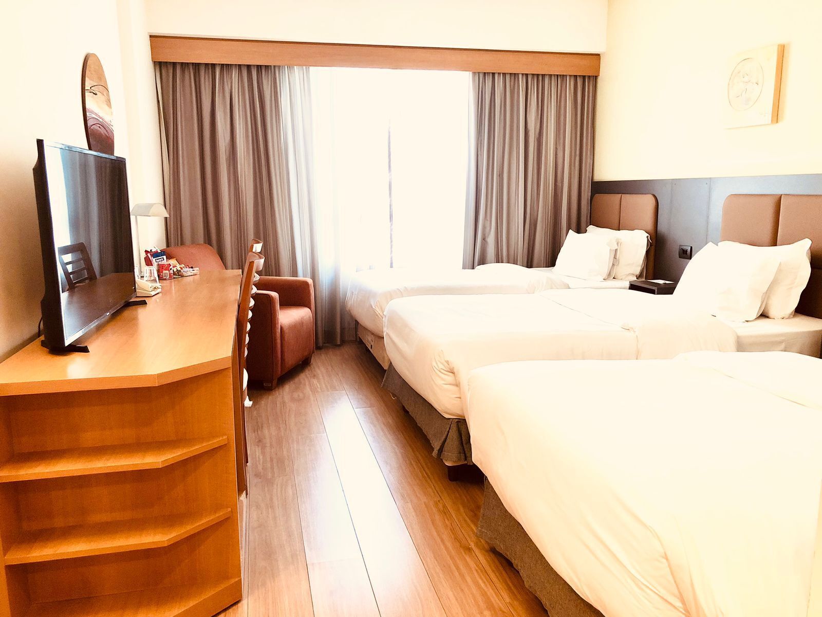 A hotel room with a desk, two beds, a chair, and a television.