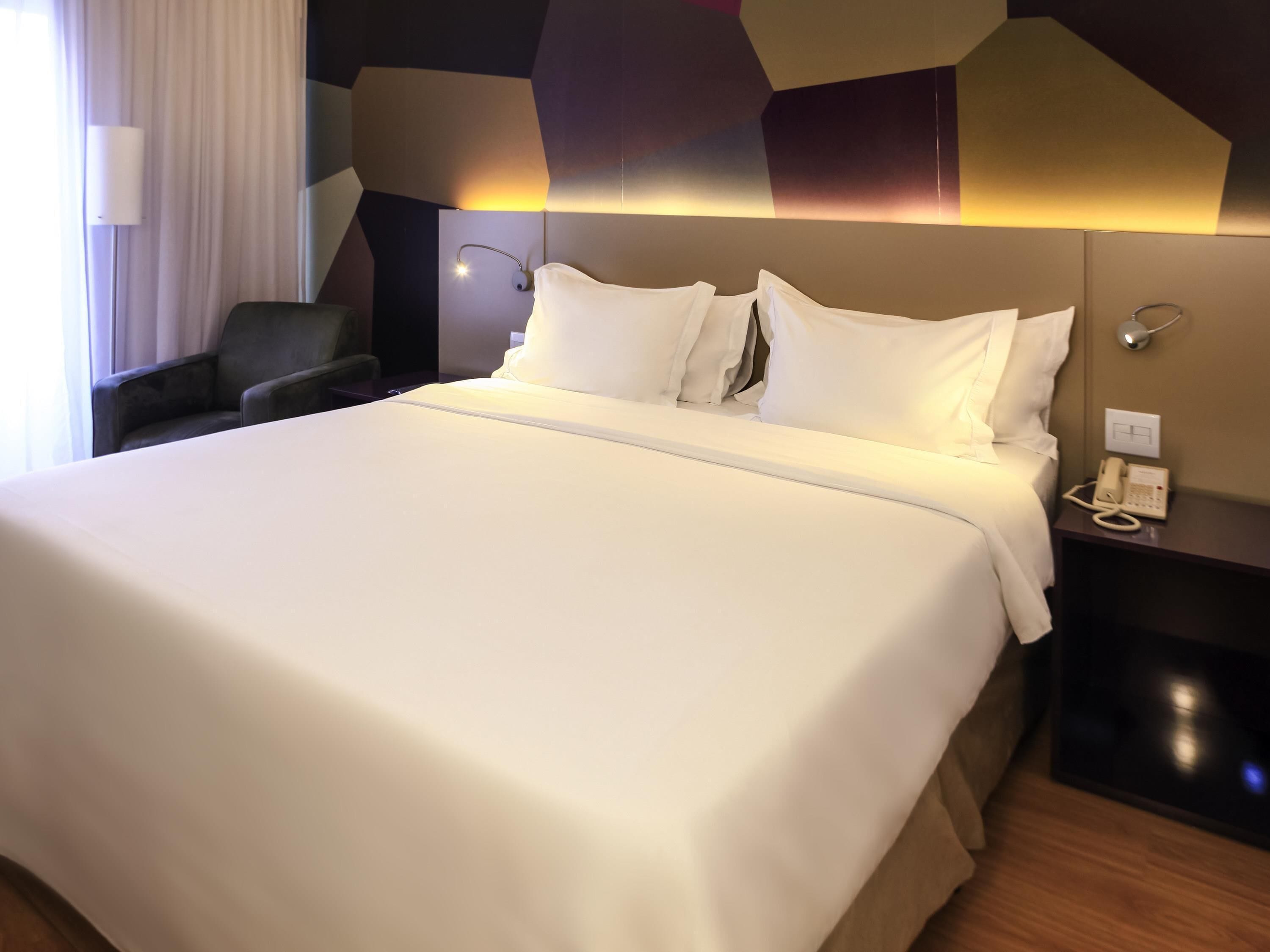 Una habitación de hotel con una cama grande, un teléfono en la mesita de noche y una silla.