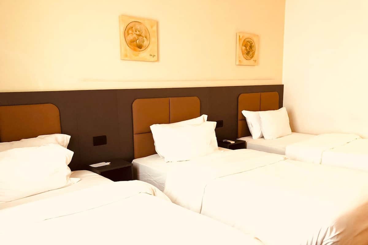 A hotel room with three beds, each with white bedding and pillows. There are two wall-mounted artworks above the beds.