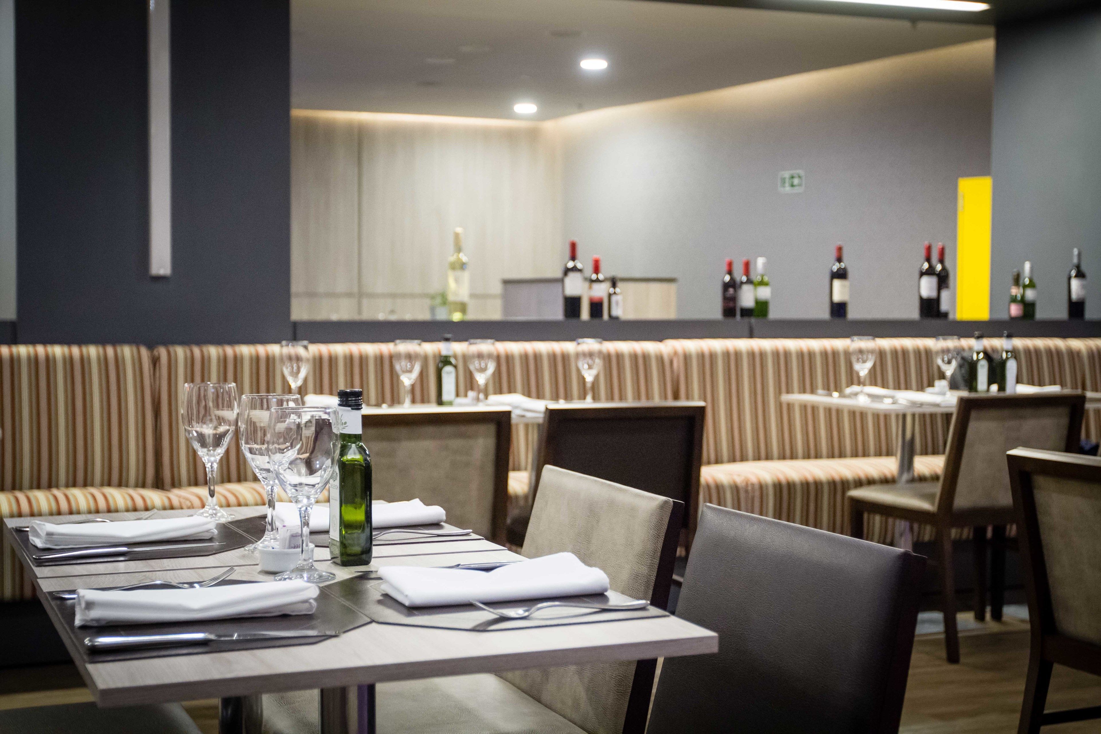 Un restaurant amb taules preparades per dinar, una zona de bar amb ampolles de vi i seients amb coixins estampats.