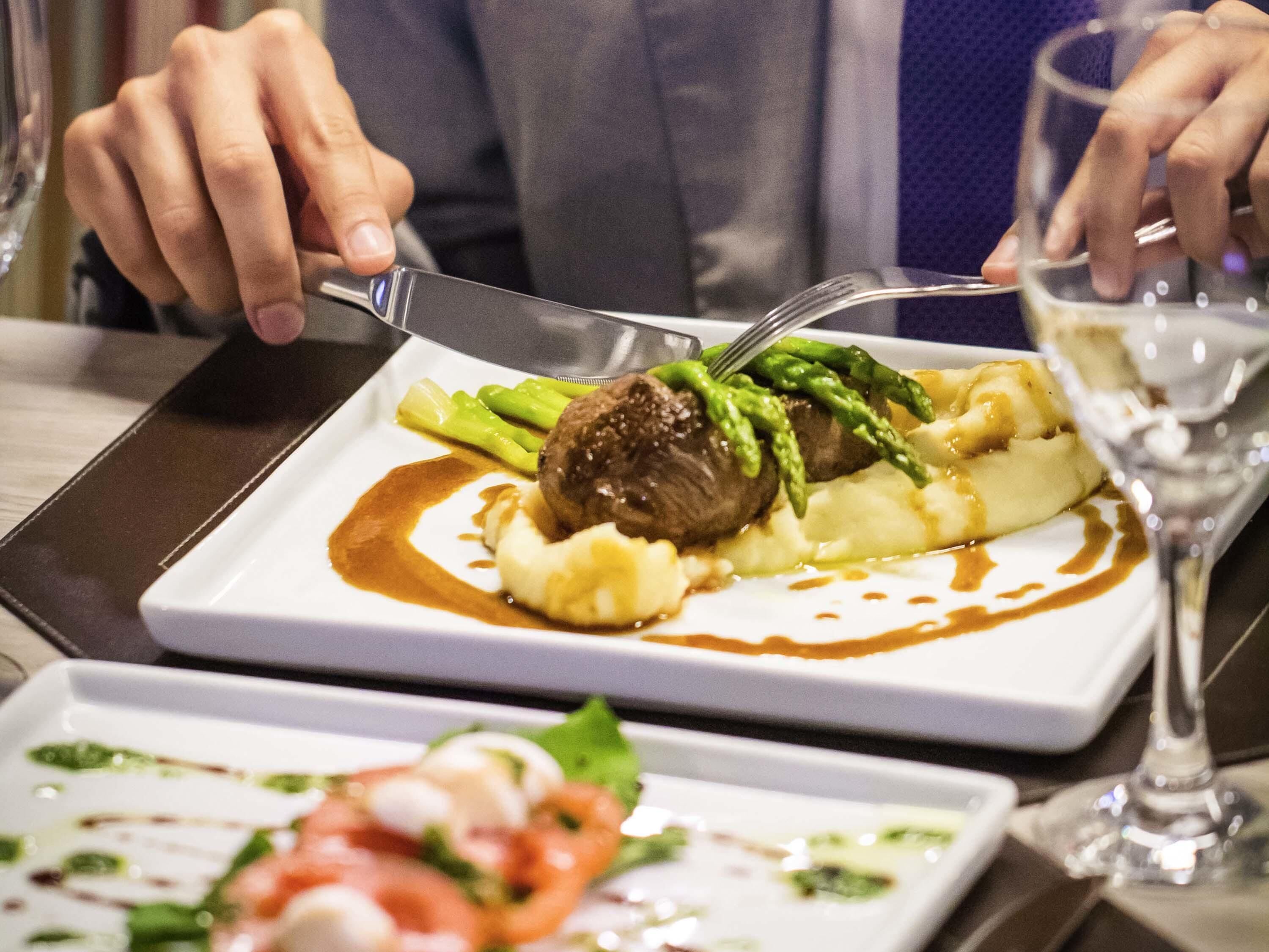 Una persona comiendo en un restaurante, con un plato de comida, un tenedor y una copa de vino.