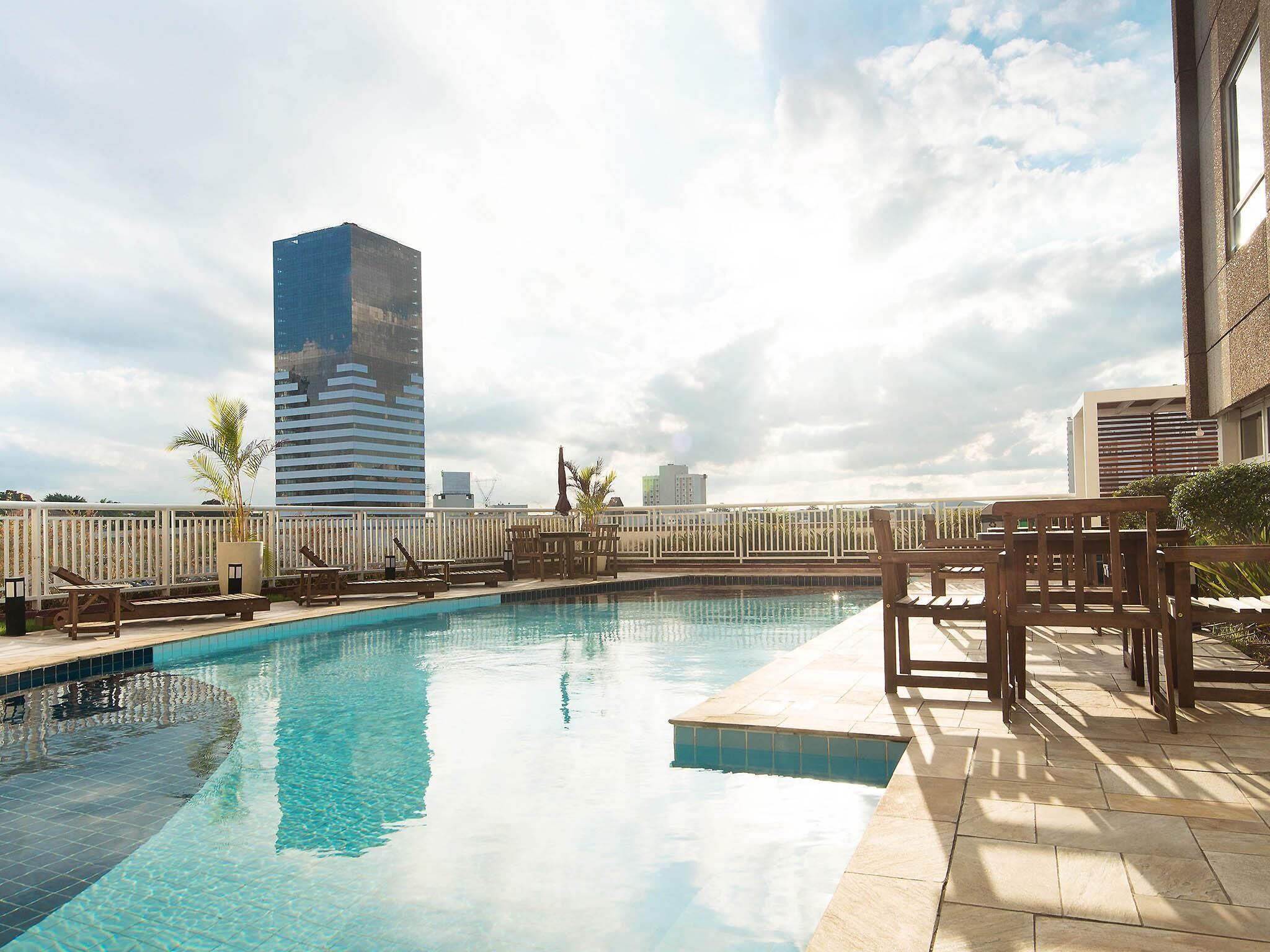 A rooftop pool with lounge chairs, a view of a tall building, and a clear sky.
