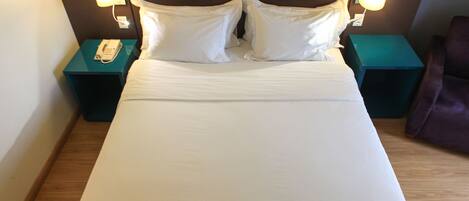A neatly made bed with white linens, two bedside tables with lamps, and a purple chair.