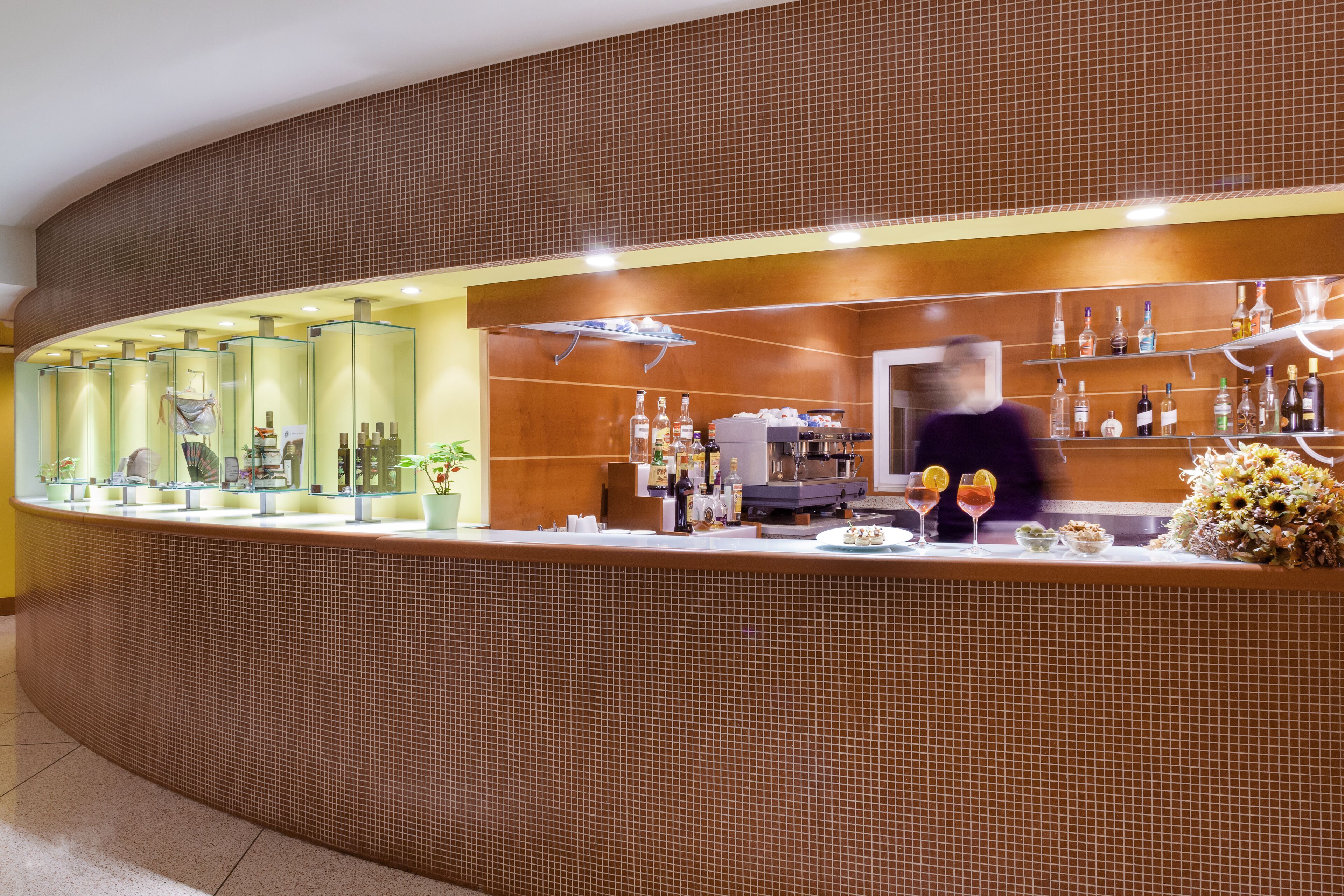 A modern bar area with a curved counter, glass display cases, and a variety of bottles and glasses.