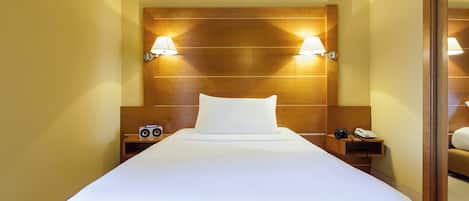 A hotel room with a large bed, wooden headboard, bedside lamps, a nightstand with a camera and phone, and a mirror.