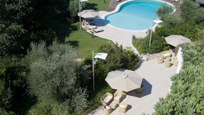Vista aérea de una piscina rodeada de sillas de descanso y sombrillas, con un área de patio y vegetación.