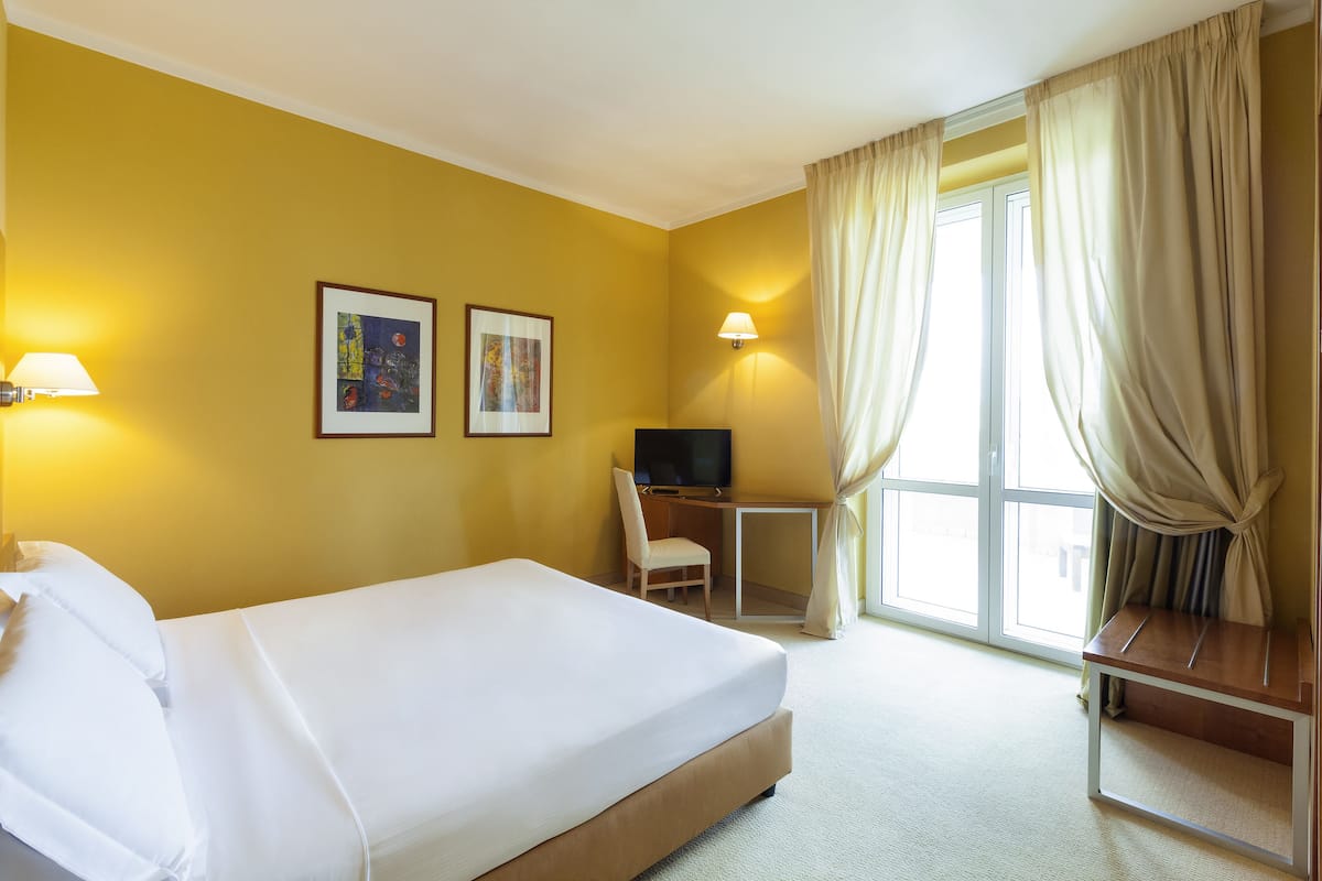 A hotel room with a bed, a desk, a chair, a TV, and two framed pictures on the wall.