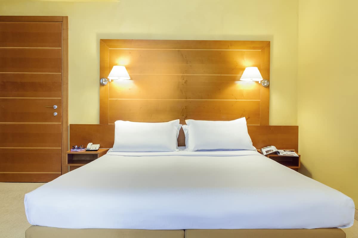A hotel room with a large bed, two bedside lamps, a wooden headboard, a nightstand with a phone, and a door.