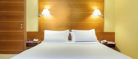 Habitación de hotel con una cama grande, dos lámparas de noche, un cabecero de madera, una mesita de noche con un teléfono y una puerta.