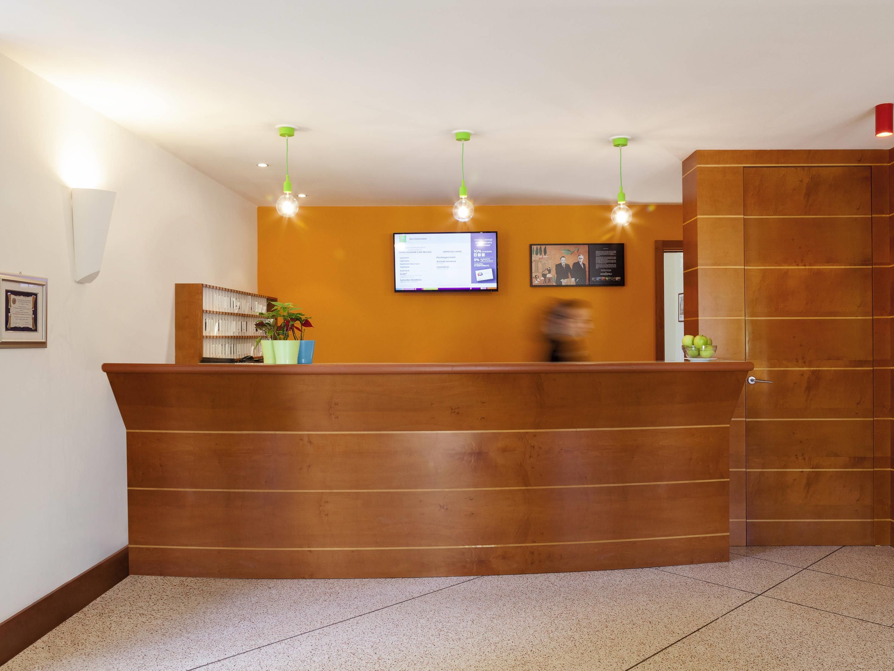 Un mostrador de recepción con una pantalla digital, un certificado enmarcado y una planta.