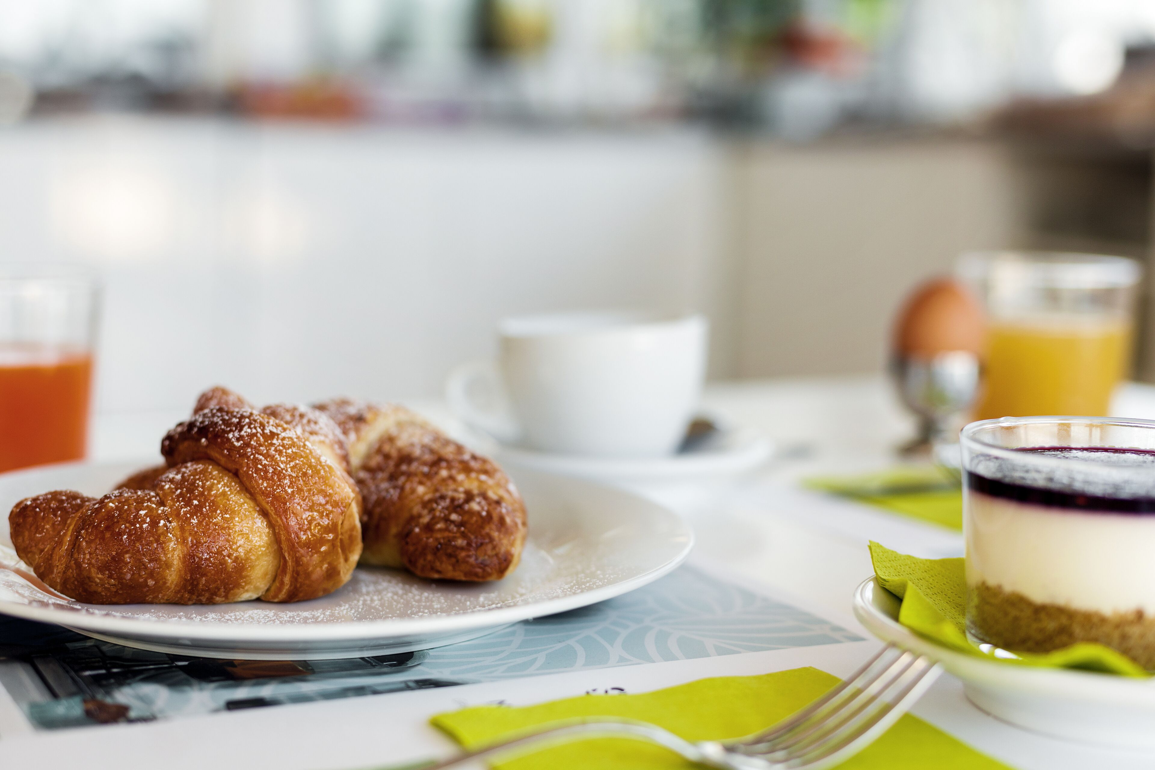 Une table dressée pour le petit-déjeuner, avec des croissants, un verre de jus d’orange et un dessert à plusieurs couches.