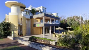 Un hotel moderno con varios balcones, mobiliario exterior y un patio ajardinado.