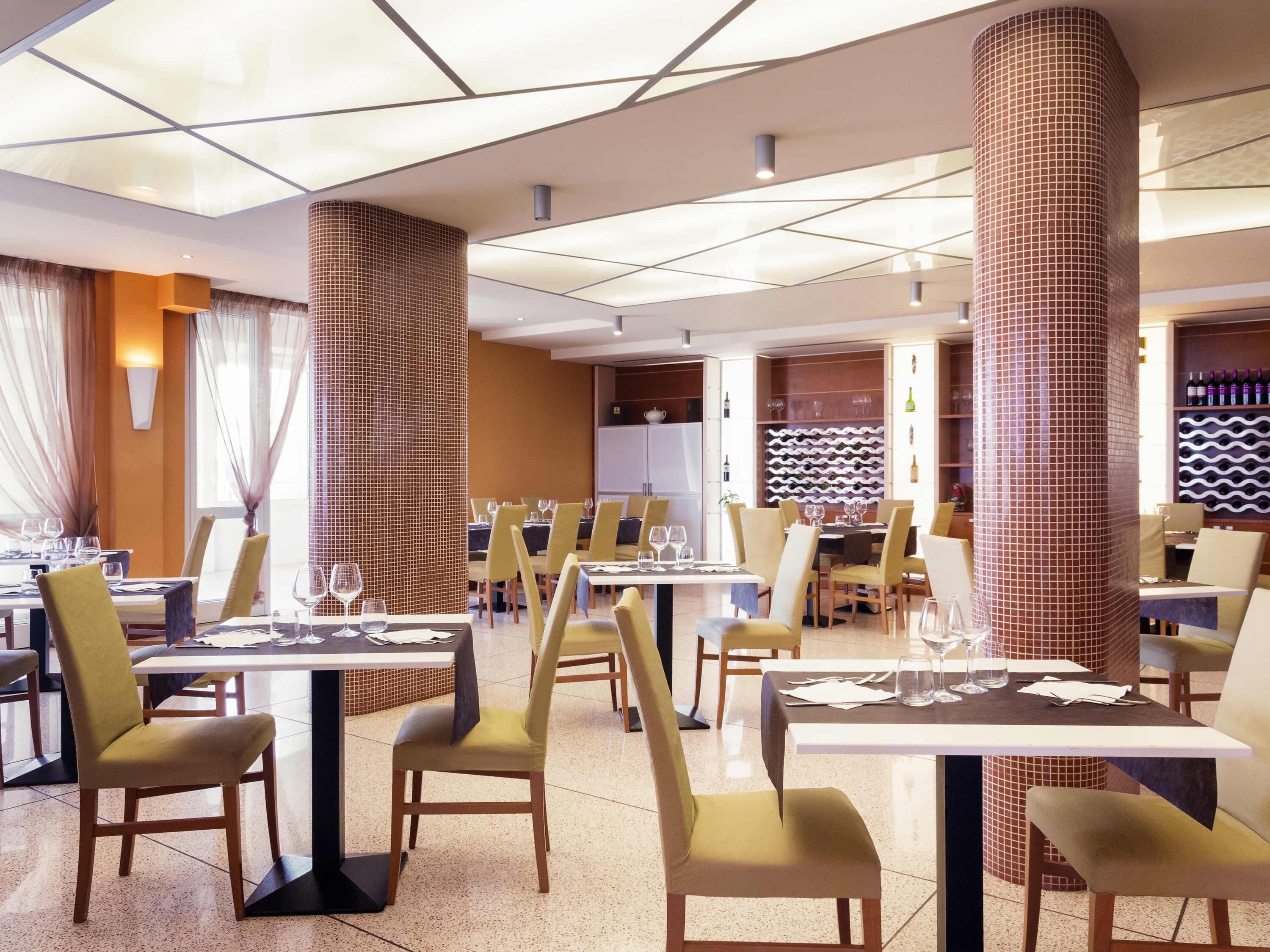 Un ristorante con diversi tavoli e sedie, una colonna in maiolica e una cantina vini sullo sfondo.