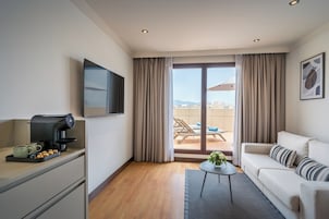 Ett modernt hotellrum med ett litet kök, en soffa, en kaffemaskin och en balkong med utsikt.