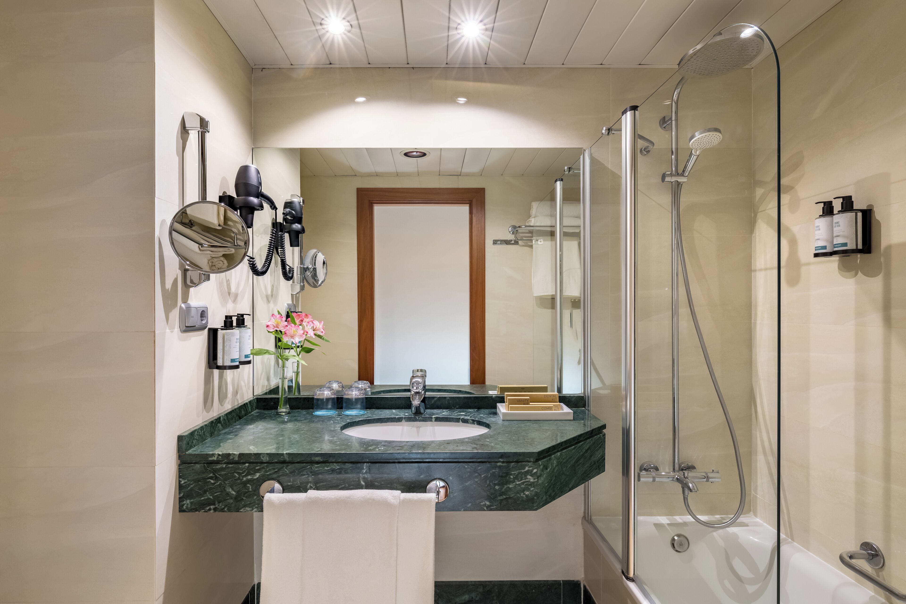 Un baño moderno con lavamanos de mármol, cabina de ducha con mampara de vidrio y espejo con secador de pelo.